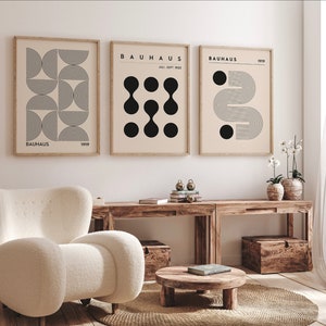 Puede incluir: Tres impresiones geom&eacute;tricas en blanco y negro enmarcadas con el texto "BAUHHAUS" y el a&ntilde;o "1919" en cada impresi&oacute;n. Las impresiones est&aacute;n colgadas en una pared blanca sobre una mesa de madera con un sill&oacute;n blanco y una peque&ntilde;a mesa de madera delante.