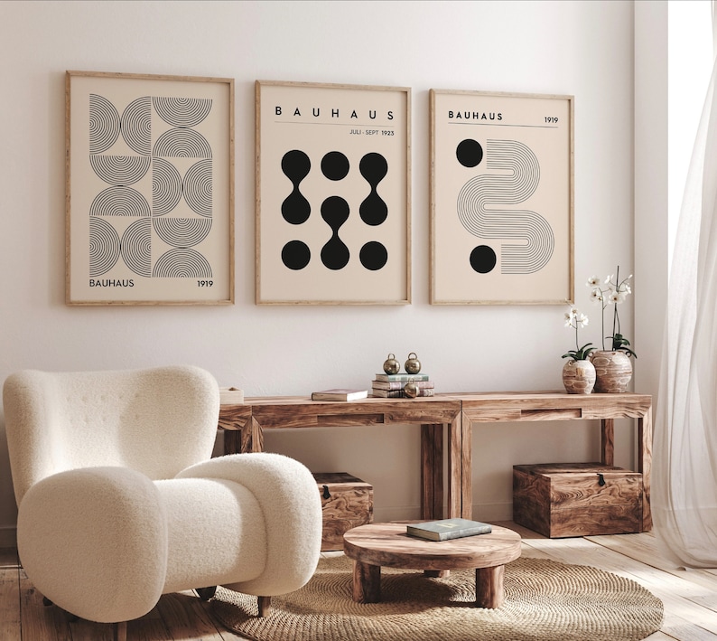 Puede incluir: Tres impresiones geom&eacute;tricas en blanco y negro enmarcadas con el texto "BAUHHAUS" y el a&ntilde;o "1919" en cada impresi&oacute;n. Las impresiones est&aacute;n colgadas en una pared blanca sobre una mesa de madera con un sill&oacute;n blanco y una peque&ntilde;a mesa de madera delante.