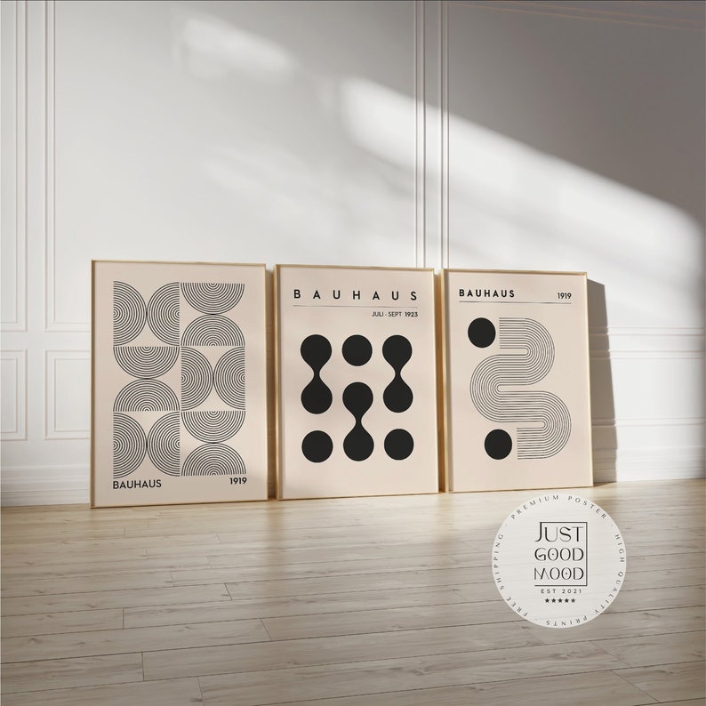 Puede incluir: Tres impresiones de arte Bauhaus minimalistas en blanco y negro con formas geom&eacute;tricas sobre un fondo beige. Las impresiones est&aacute;n enmarcadas en oro y tienen el texto "BAUHAUS" y "1919".