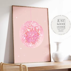 Könnte beinhalten: Gerahmtes rosa Poster mit einem Discokugel-Design. Die Discokugel besteht aus kleinen, quadratischen, rosa und weißen Kacheln. Der Hintergrund ist einfarbig hellrosa mit weißen Sternakzenten. Der Text "JUST GOOD MOOD" befindet sich in einem weißen Kreis.