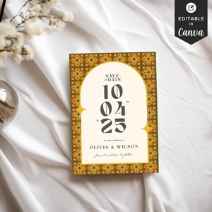 May include: A wedding invitation card with a decorative border and an arched design. The card features the text "SAVE THE DATE" and the date "10/04/25" along with the names "OLIVIA & WILSON". The card is set against a white fabric background.