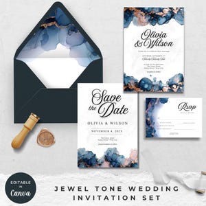 May include: A jewel-toned wedding invitation set featuring navy blue and gold watercolor designs. The set includes an invitation, RSVP card, and a "Save the Date" card. An envelope, wax seal, and wooden stamp are also included.