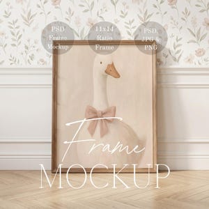 May include: A framed print featuring a watercolor illustration of a goose with a pink bow. The artwork is set in a wooden frame and is labeled "11x14 Ratio Frame". The words "Frame Mockup" are written across the bottom of the frame.