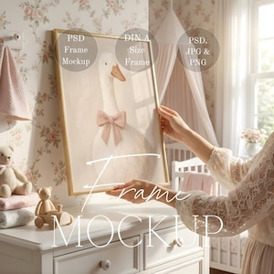 May include: A framed art print featuring a watercolor illustration of a white goose with a pink bow. The artwork is displayed in a gold frame. The image is a mockup, with text indicating PSD frame mockup, DIN A size frame, and PSD, JPG & PNG.