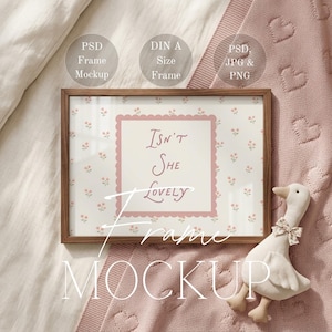 Puede incluir: Maqueta de marco con el texto "Isn't She Lovely" sobre un fondo floral. El marco es marrón, con un pato de peluche y una manta rosa.