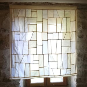 Peut inclure: Un rideau blanc avec un motif géométrique de lignes brunes créant des carrés et des rectangles. Le rideau est suspendu à une fenêtre avec un mur en pierre derrière.
