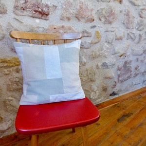 Peut inclure: Une chaise rouge avec un coussin en patchwork blanc et gris. La chaise est devant un mur en pierre.