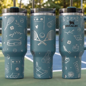 Three blue tumblers with tennis-themed designs and the Stanley logo printed on them.