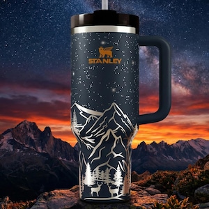 A stainless steel thermos mug with a mountain landscape design, set against a night sky with stars and a colorful sunset.