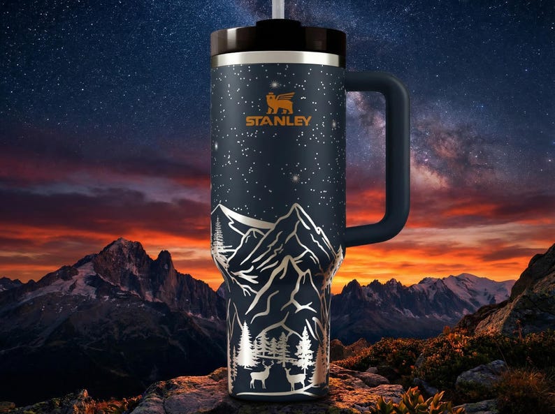 A stainless steel thermos mug with a mountain landscape design, set against a night sky with stars and a colorful sunset.