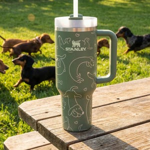 A stainless steel thermos with a handle and lid sits on a wooden picnic table, with several dogs playing in the background.