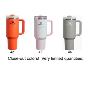 three different colored Stanley tumblers, each with a unique color: orange, pink, and gray.