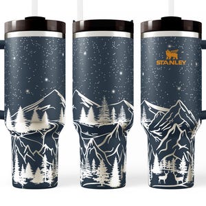 A set of three black insulated tumblers with a mountain landscape design printed on them.