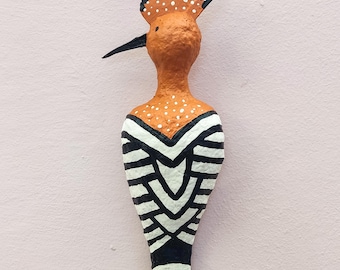 Può includere: Scultura di uccello artigianale dal design distintivo. L'uccello presenta un corpo arancione con pois bianchi, un becco nero e una cresta con dettagli neri e bianchi. Il corpo è decorato con strisce bianche e nere.