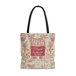 May include: Tote bag with a red and cream toile pattern featuring a classical design. The bag has black handles and a rectangular label with the text "Mozart The Marriage of Figaro" in a decorative font.