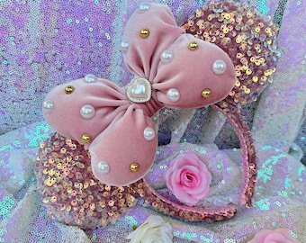 Peut inclure: Un serre-tête avec un nœud en velours rose orné de perles et d'accents dorés. Le serre-tête est décoré de paillettes et comporte un nœud rose avec un charme en forme de cœur.