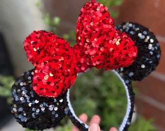 Op de afbeelding: Zwarte en rode pailletten Minnie Mouse orenband met een grote rode strik.