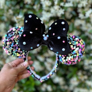 May include: Black velvet Minnie Mouse ears with iridescent sequins and a black bow with rhinestones.