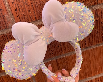 Peut inclure: Oreilles de souris Minnie blanches à paillettes irisées avec un grand nœud en velours blanc.