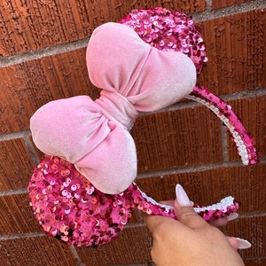 May include: Pink sequined Minnie Mouse ears headband with a large pink velvet bow.