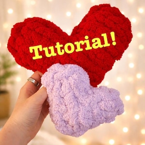 May include: A large red heart-shaped plush and a smaller light purple heart-shaped plush made of chunky yarn. The red heart features the yellow text Tutorial! across its center. Both items have a soft, textured, and looped knit appearance.