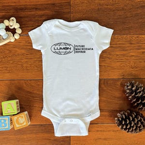 May include: White baby onesie with a black graphic of a globe with the text "LUMON" and "FUTURE MACRODTA REFINER" on the front.