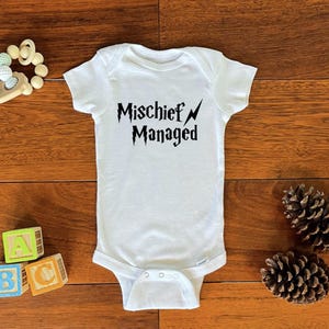 May include: White baby onesie with black text that reads "Mischeif Managed" with a lightning bolt graphic.