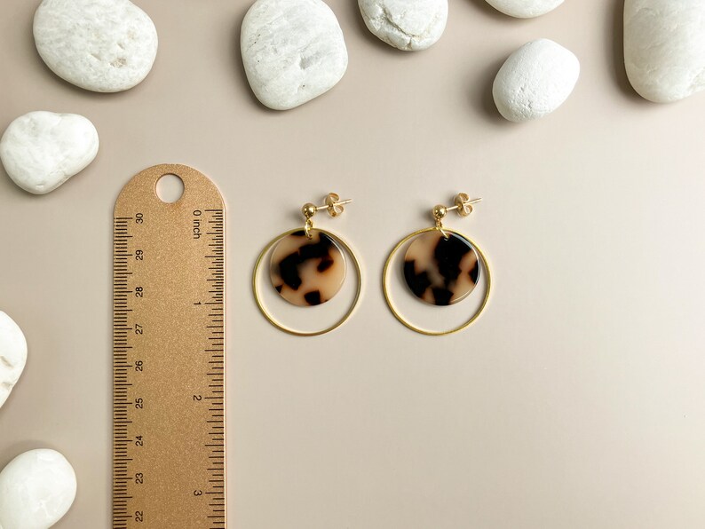 May include: Gold hoop earrings with a brown and white patterned circle pendant. The earrings are shown next to a ruler.