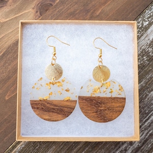 May include: A pair of gold and wood earrings with a white resin base and gold leaf accents. The earrings are in a small box.