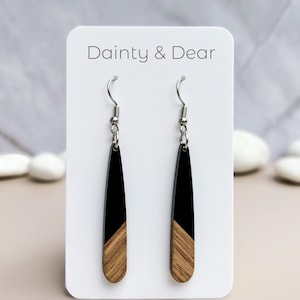 May include: Black and wood drop earrings with silver hooks. The earrings are on a white card with the text "Dainty & Dear".
