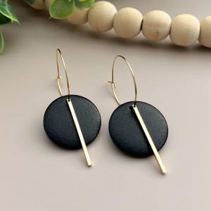 May include: A pair of black and gold hoop earrings with a circular black pendant and a gold bar hanging from the bottom.