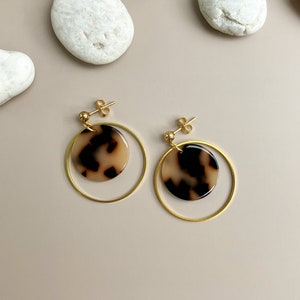 May include: A pair of gold hoop earrings with a brown and white patterned circle pendant hanging from each hoop.