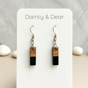 May include: A pair of wooden earrings with a black and brown color scheme. The earrings are rectangular in shape and have a silver hook.