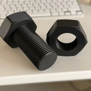 May include: A black bolt and nut set. The bolt has a hexagonal head and a threaded shaft. The nut is also hexagonal with a threaded interior. The set is made of a dark material and is suitable for construction or mechanical projects.