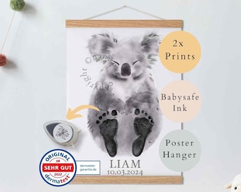 May include: A watercolor print of a koala with a baby's footprints on its belly. The print is framed and hanging on a wall. The text "Liam 10.03.2024" is printed below the koala. The print is accompanied by two ink pads and a poster hanger.