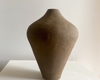 May include: A brown ceramic vase with a rounded, bulbous body and a narrow neck. The vase has a rough, textured surface.