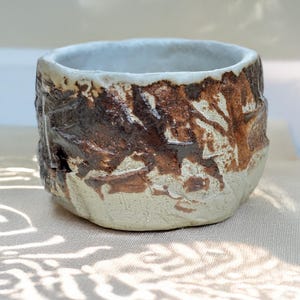 May include: A small, white ceramic bowl with a brown glaze. The glaze has a textured, rough appearance, giving the bowl a rustic look.