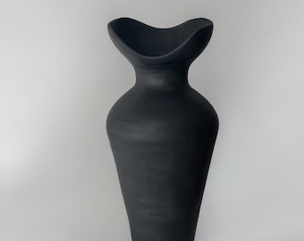 May include: A matte black ceramic vase with a unique, flared top. The vase has a slender neck that widens into a bulbous body, then tapers to a rounded base. The overall shape is elegant and modern, suitable for home decor.