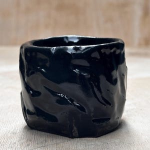 May include: A black ceramic planter with a textured, wavy surface. The planter has a glossy finish.