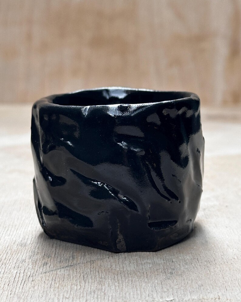May include: A black ceramic planter with a textured, wavy surface. The planter has a glossy finish.