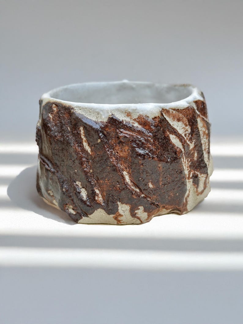 May include: A small, white ceramic planter with a rough, textured surface and brown glaze. The planter has a rounded shape and is perfect for displaying small plants or succulents.