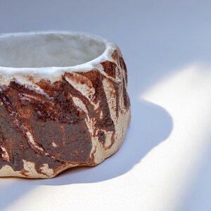 May include: A small, white ceramic planter with a brown glaze. The glaze has a textured, organic pattern.