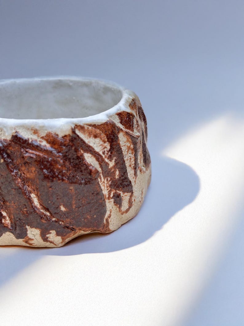 May include: A small, white ceramic planter with a brown glaze. The glaze has a textured, organic pattern.