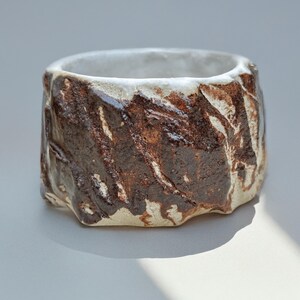 May include: A white ceramic planter with a brown glaze, featuring a textured, rough surface. The planter has a wide, round opening and a slightly rounded base.