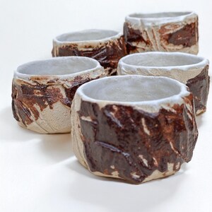 May include: Set of five small ceramic bowls with a white glaze and brown accents. The bowls have a rough, textured surface.