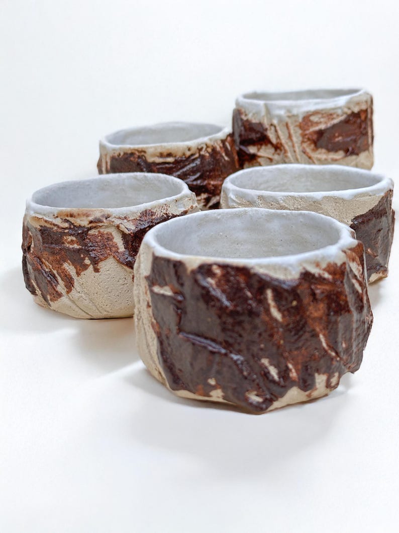 May include: Set of five small ceramic bowls with a white glaze and brown accents. The bowls have a rough, textured surface.