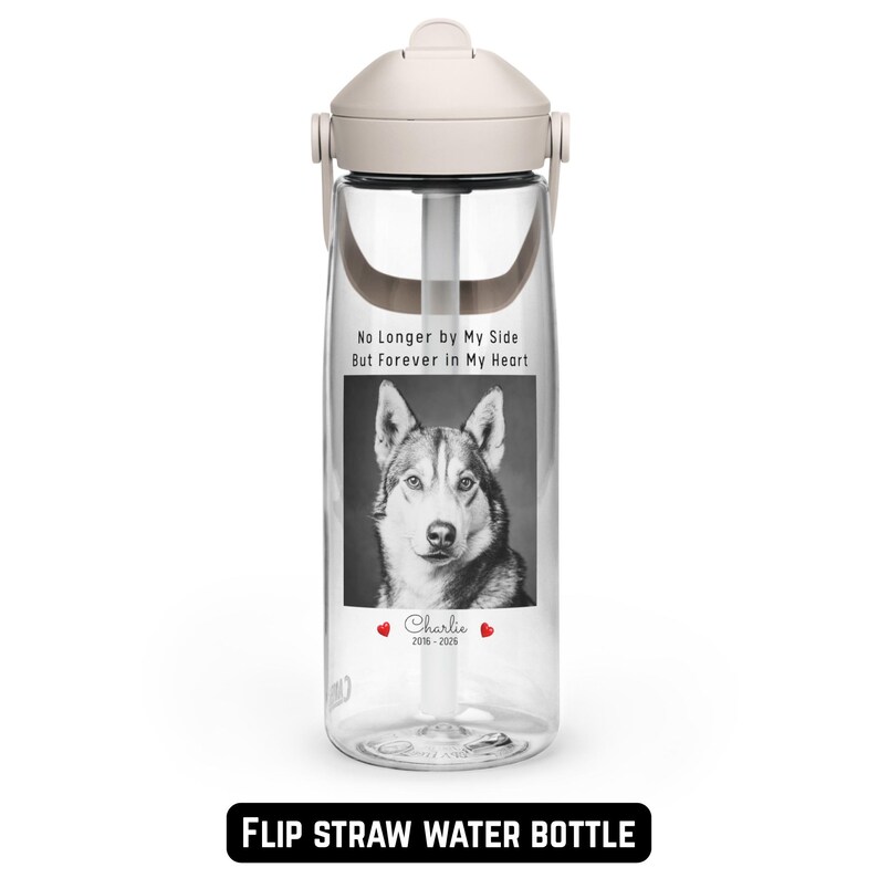 May include: Clear flip straw water bottle with a cream-colored lid and handle. The bottle features a black and white image of a dog with the text "No Longer by My Side But Forever in My Heart" and the name "Charlie" with dates.