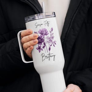 Könnte beinhalten: Weißer isolierter Becher mit Henkel, transparentem Deckel und Strohhalm. Der Becher hat ein Blumendesign in Lilatönen und den Text "Season Fifty" und "Brittany".
