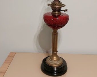 May include: A red glass oil lamp with a brass base and a clear glass chimney. The lamp has a decorative, diamond-shaped pattern on the glass.