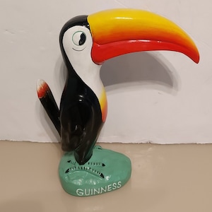 May include: A black and white toucan figurine with a yellow and red beak, standing on a green base with the word "GUINNESS" printed on it.